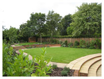 Sloping garden contoured into comfortably flat areas.  Curved steps rise from main patio to a large lawn, with small circular patio backed by a curved wall.